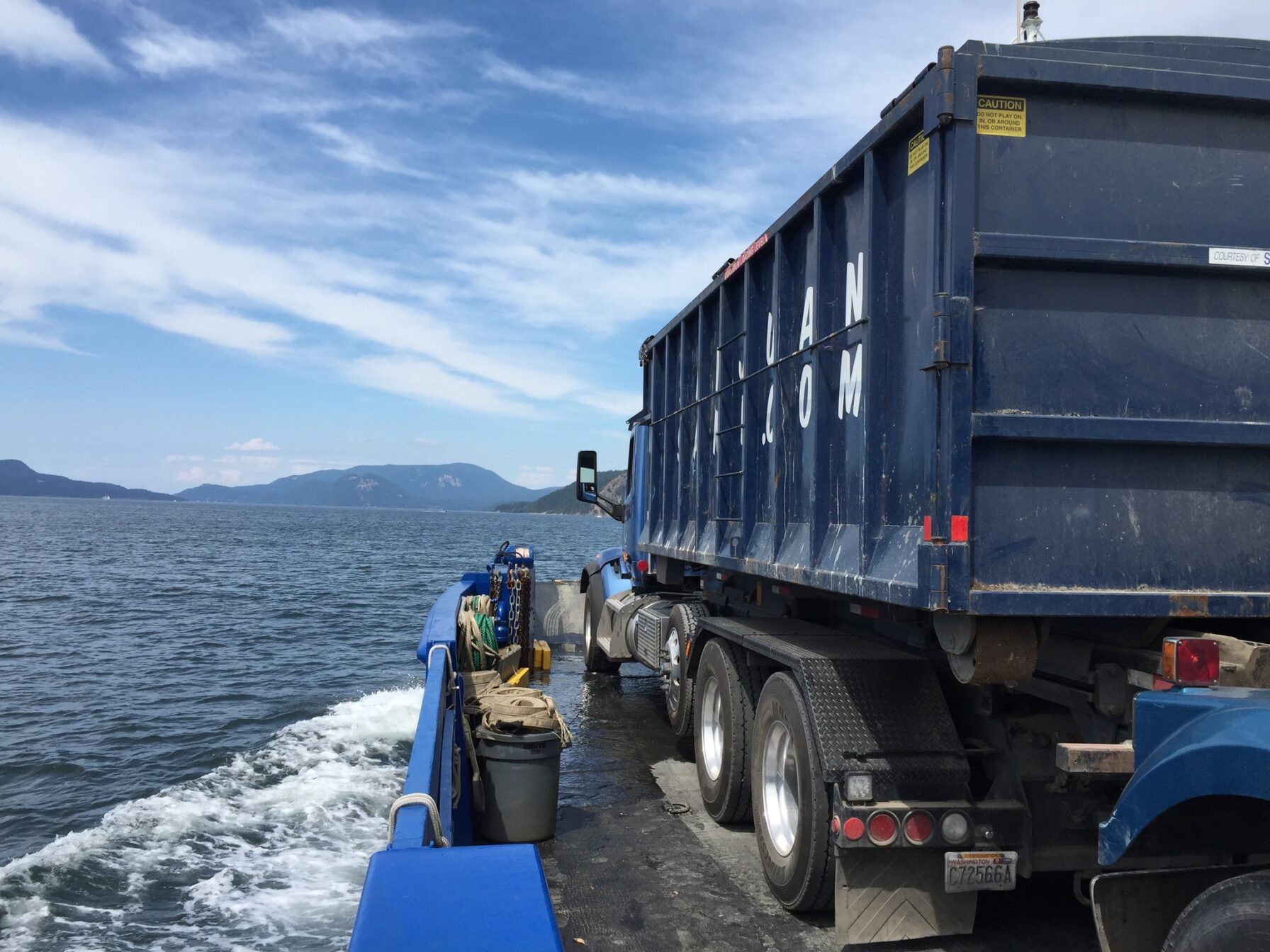 blue garbage truck sitting on a barge in the water